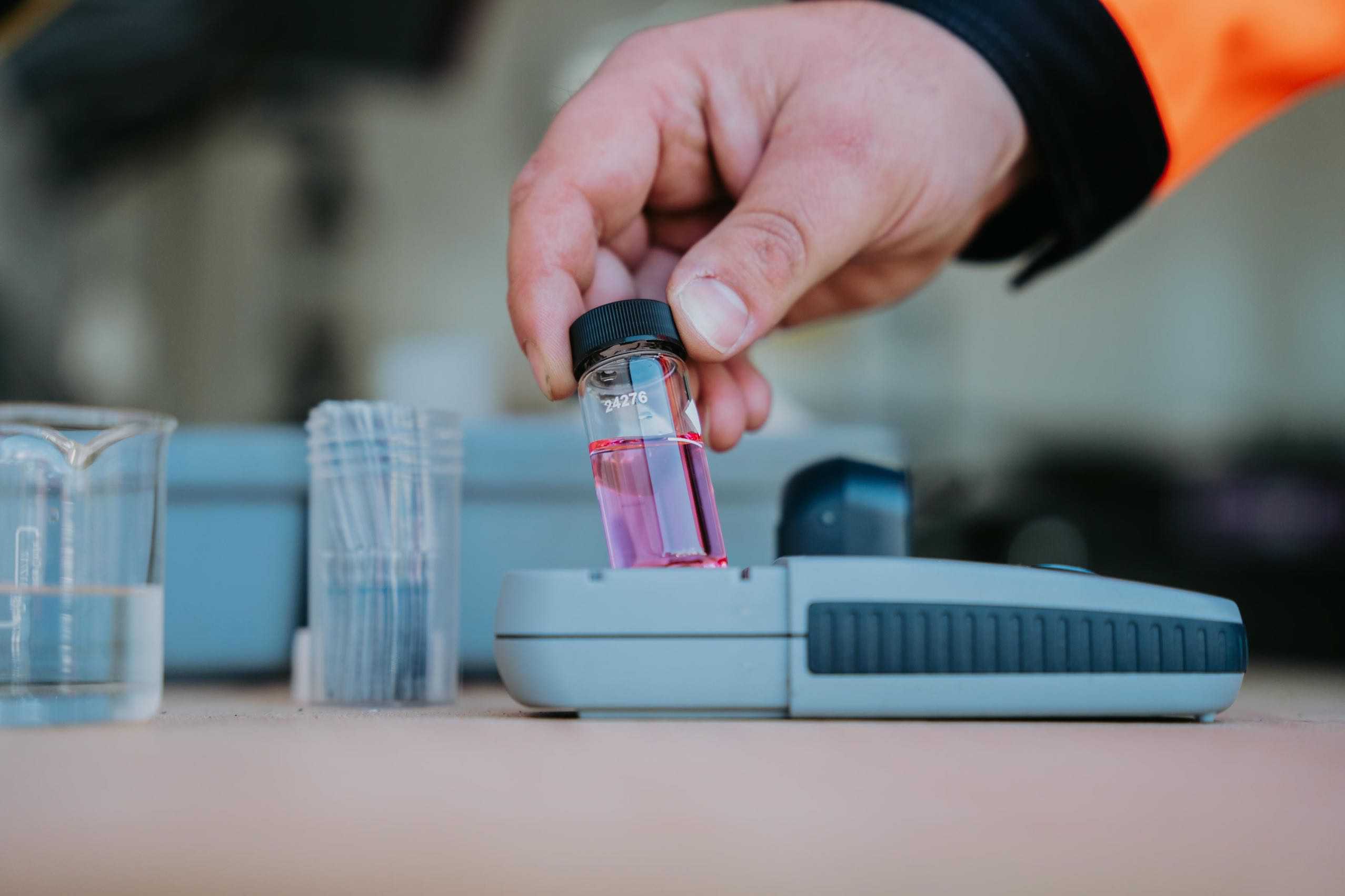 Die Hand eines Mitarbeiters an einer Laborprobe. Im Glasbehälter befindet sich eine gefärbte Flüssigkeit